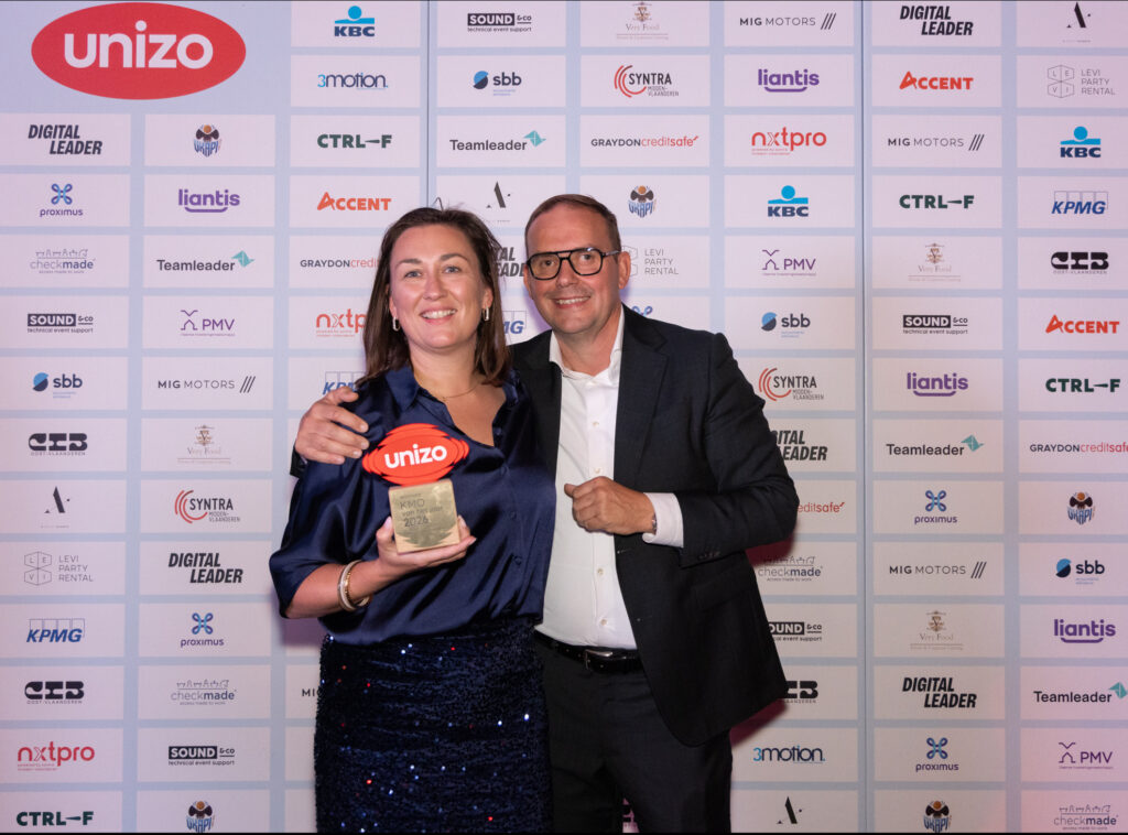 Kelly Van Landeghem en Frederik Smet met de Unizo Award van KMO van het Jaar Oost-Vlaanderen, poserend voor de logo's van de partners van Unizo