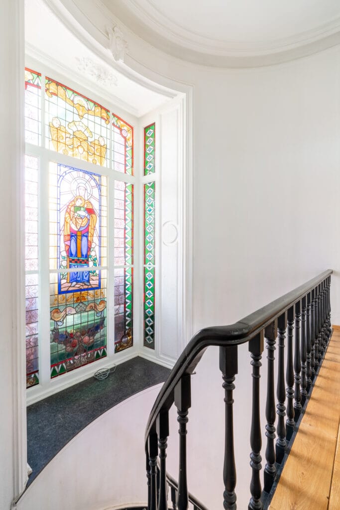 Detail traphal met glas in loodramen, houten trap en parketvloeren
